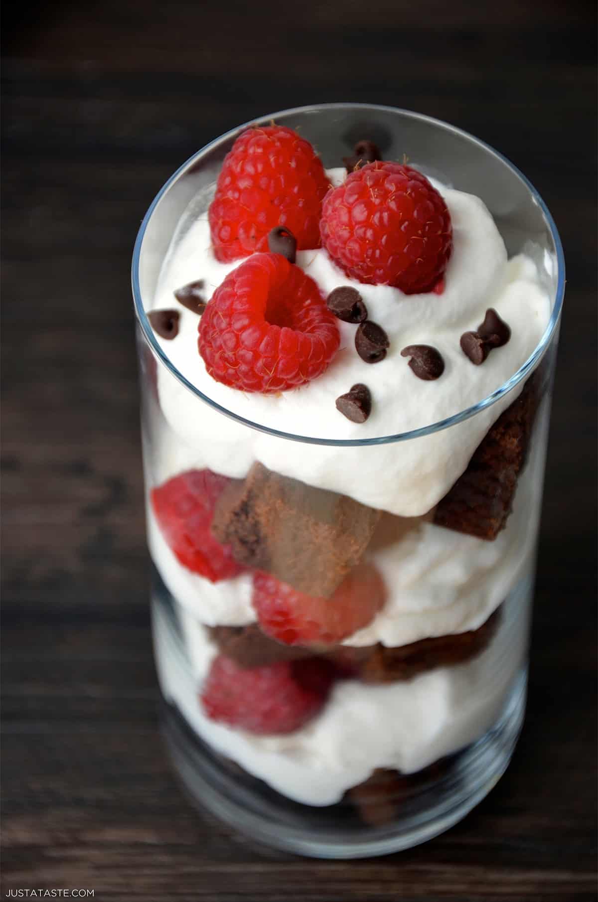 A dessert cup filled with brownie pieces, fresh raspberries, whipped cream and mini chocolate chips. 