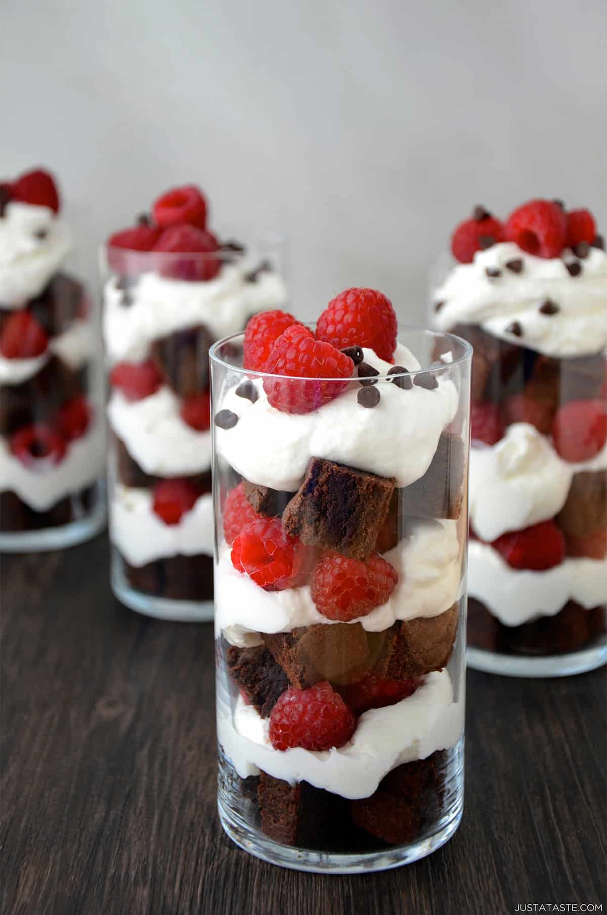 A dessert cup with layers of brownie chunks, whipped cream and fresh raspberries topped with mini chocolate chips.