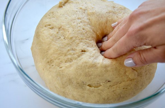 Hand poking cinnamon roll dough in clear bowl