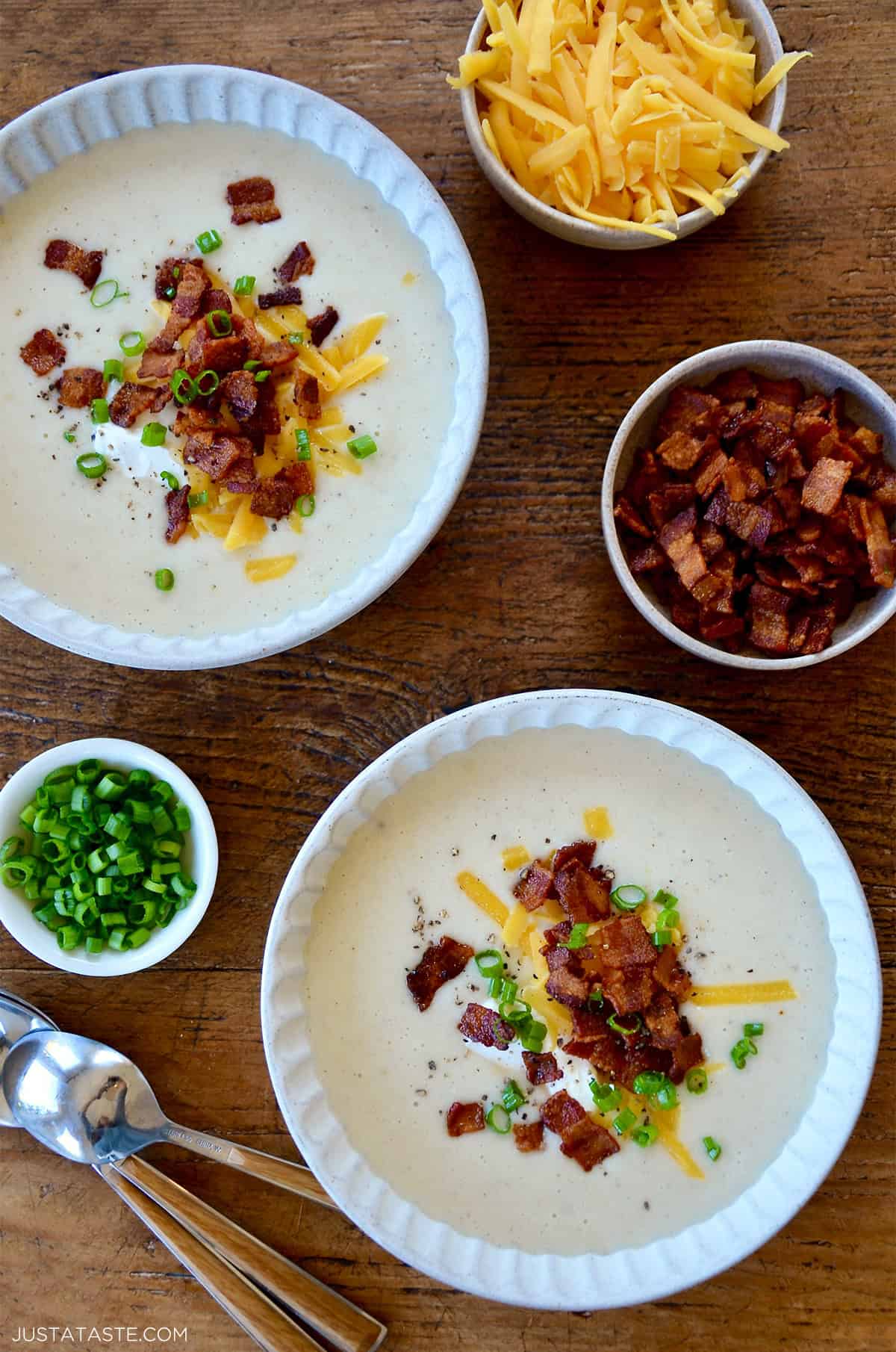 Two bowls containing creamy potato soup topped with crispy bacon, shredded cheddar cheese, a dollop of sour cream and sliced green onions.