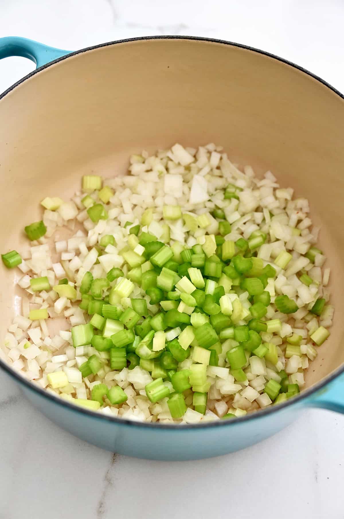 A Dutch oven containing sautéed diced onions and celery in bacon grease.