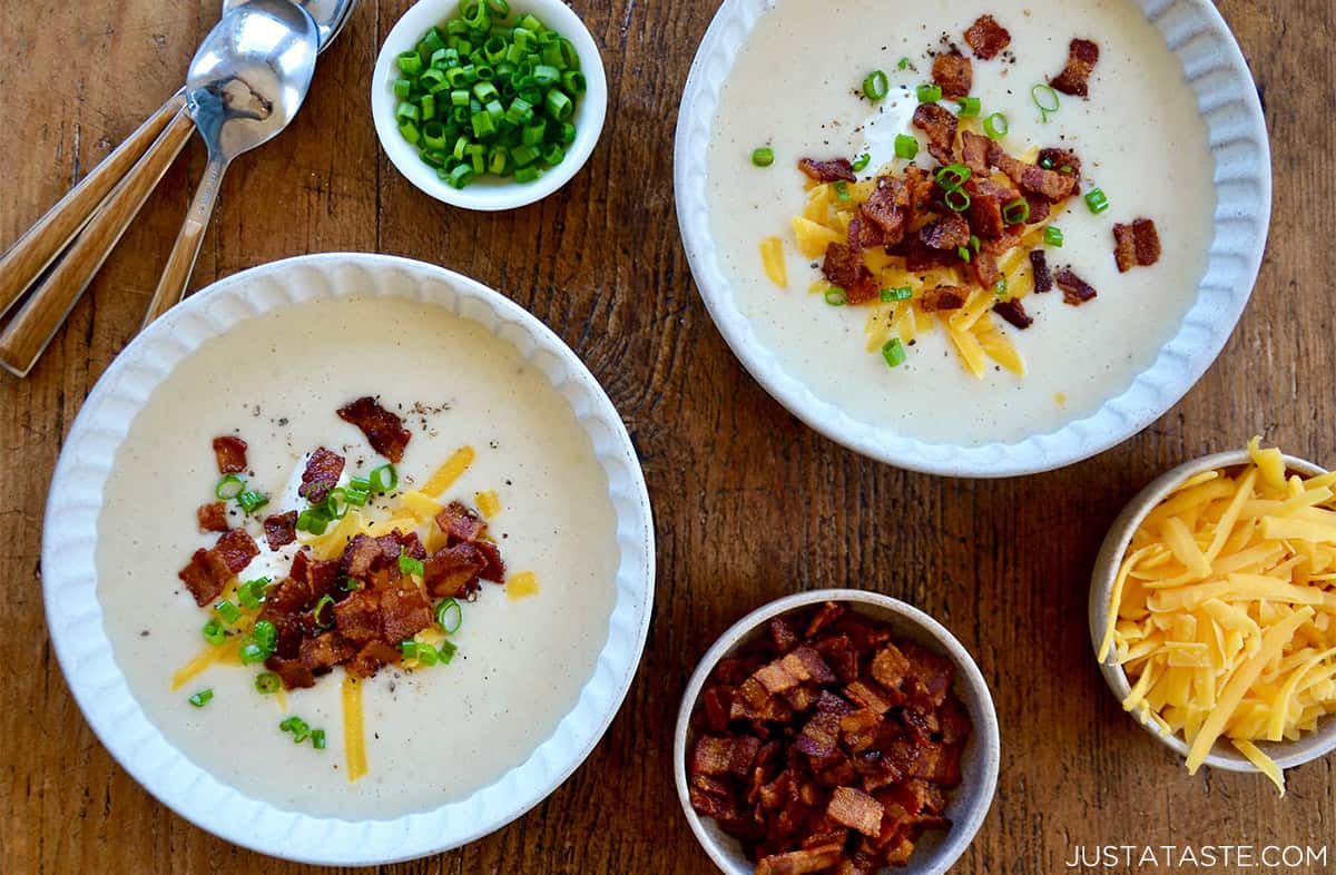 Two bowls containing loaded baked potato soup with crispy bacon, shredded cheese, scallions and sour cream as garnishes.