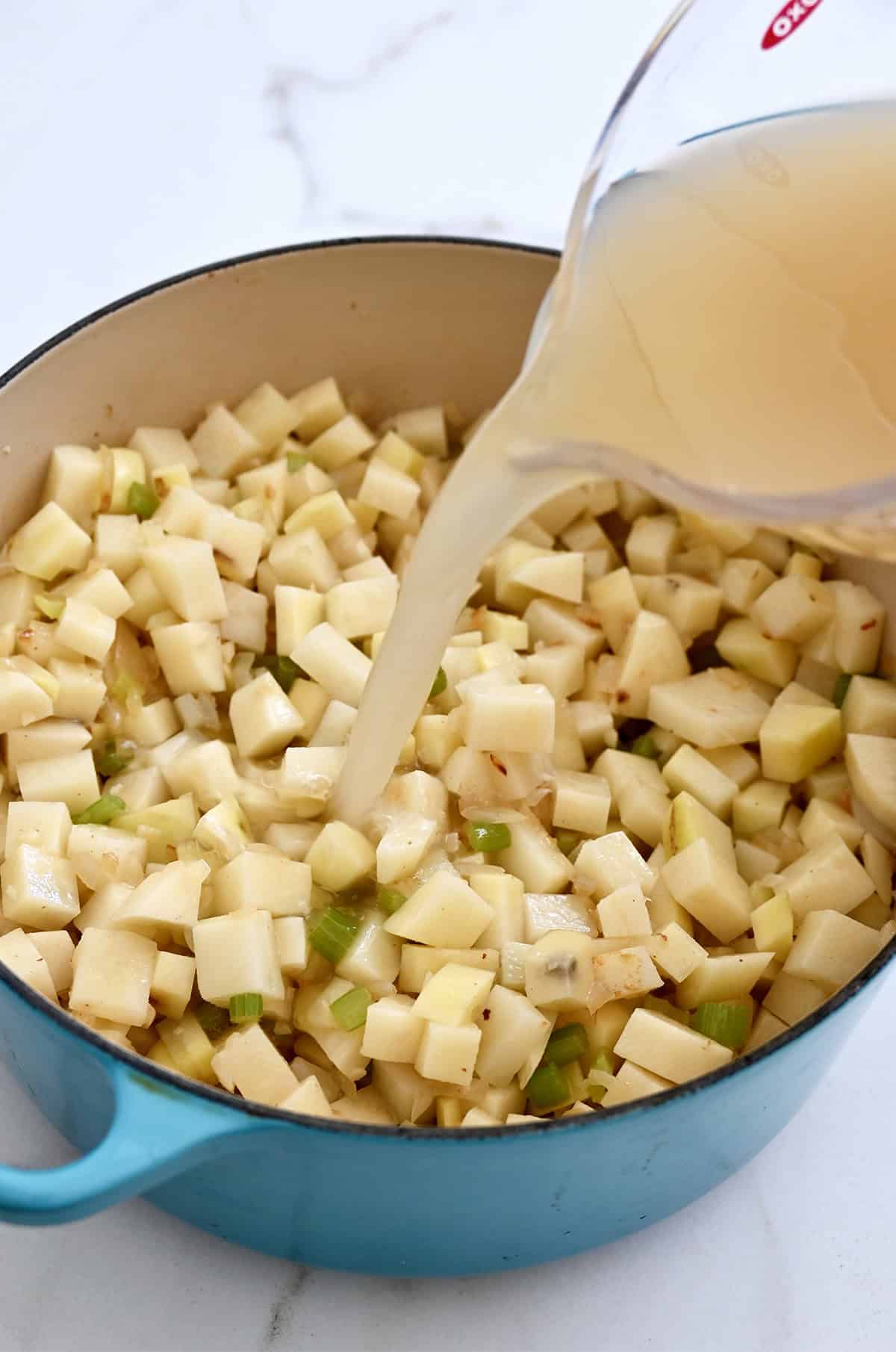 Diced potatoes and stock being added to a large heavy-bottomed pot.