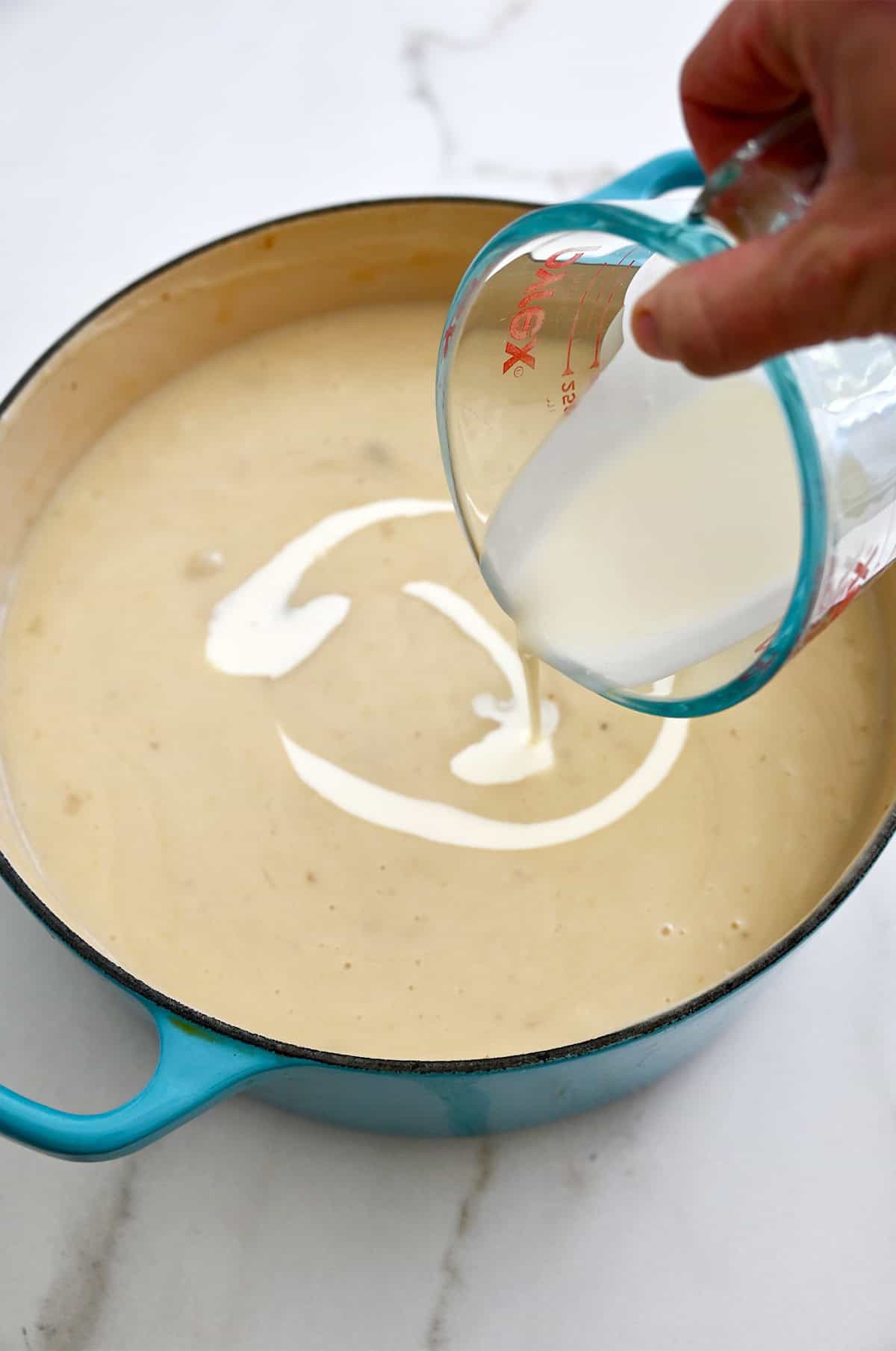 Heaving cream being stirred into a pot of creamy potato soup.