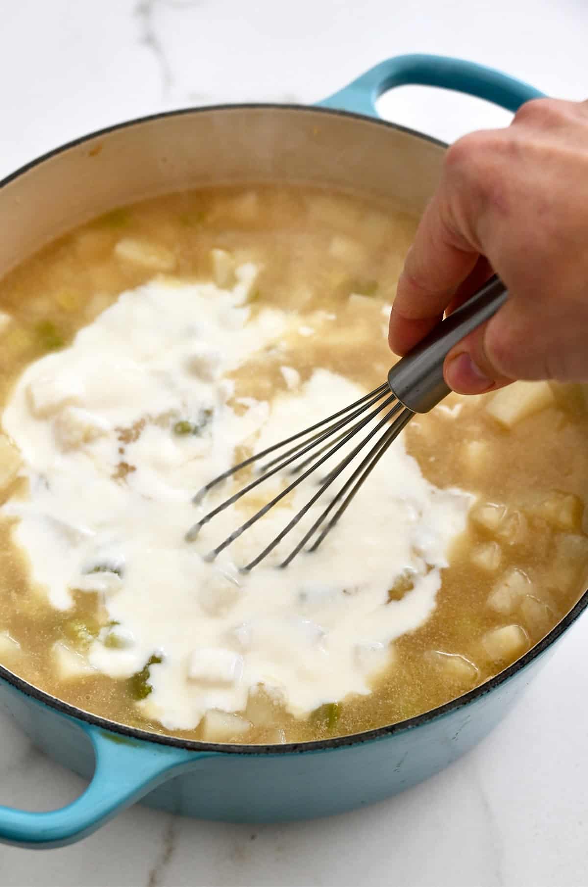 Whisking a roux into a pot of potato soup.